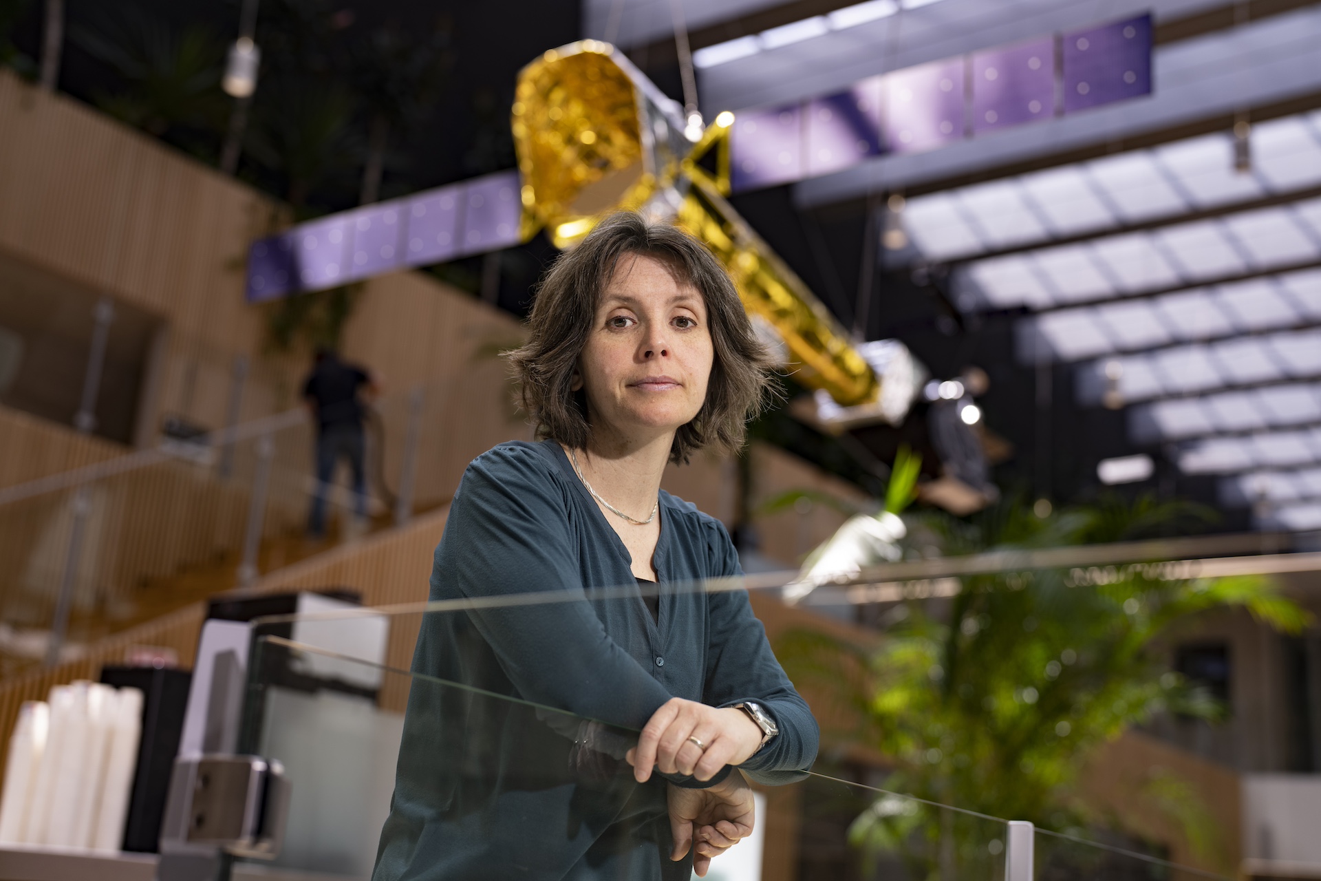 A female x-ray astrophysics scientist, Elisa Costantini, posing in front of an X-ray telescope model that hangs from the ceiling of a spaceous atrium, in the building of Space Research Organisation Netherlandss in Leiden.