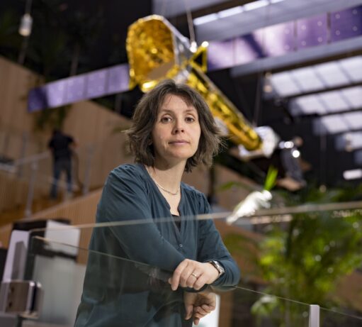 A female x-ray astrophysics scientist, Elisa Costantini, posing in front of an X-ray telescope model that hangs from the ceiling of a spaceous atrium, in the building of Space Research Organisation Netherlandss in Leiden.